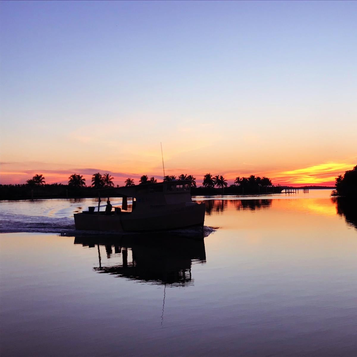Fishing Boat on a calm lake at sunset with palm trees in the background